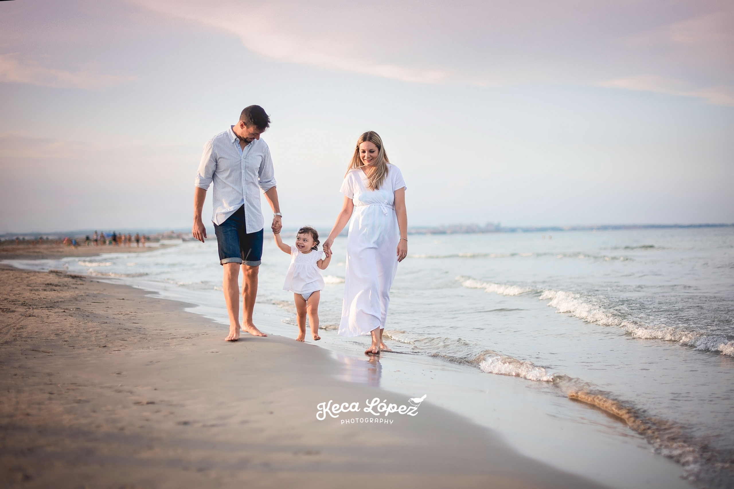 Familia paseando por la orilla de la playa. Vestido blanco