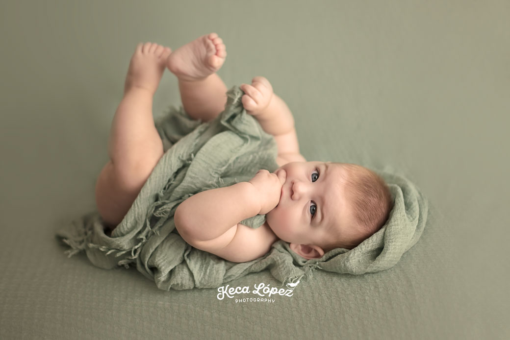 Bebé de 7 meses con ojos azules. Fondo verde y mantita verde