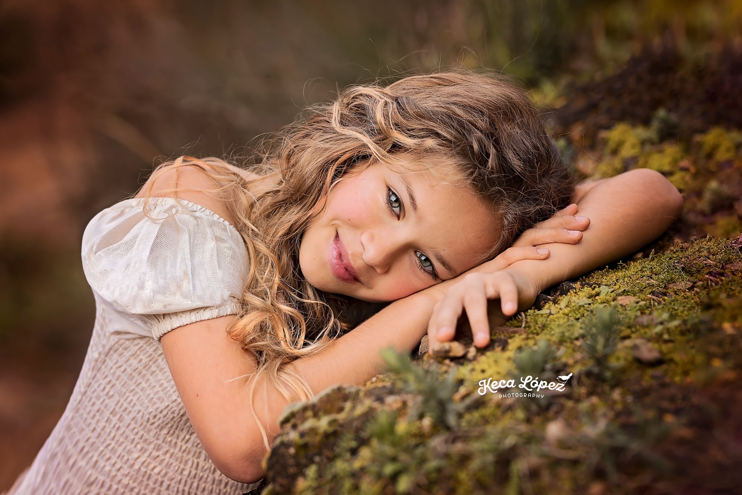 Niña de ojos azules sobre roca cubierto de musgo