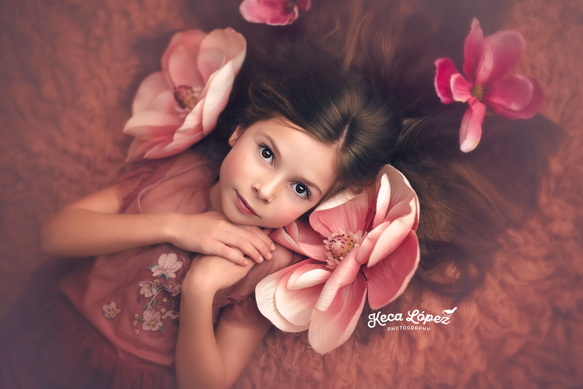 La niña está tumbada sobre una lecho de flores rosas, su mirada es penetrante.