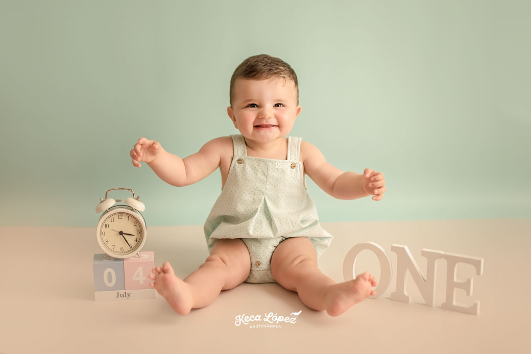 Bebé sonriendo con la fecha de su cumpleaños y en letras de madera la palabra ONE